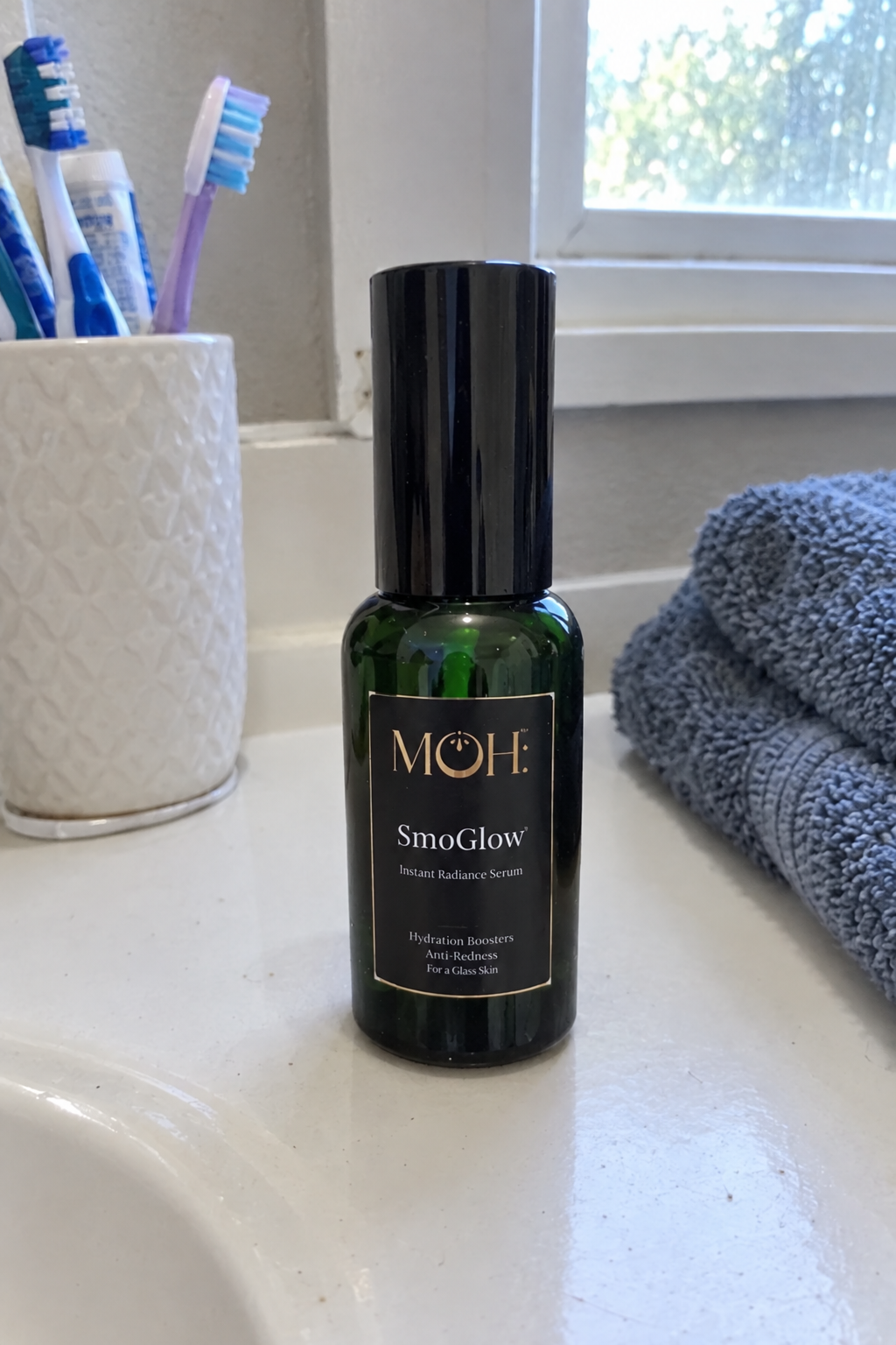 SmoGlow on a bathroom counter beside a toothbrush cup and towel